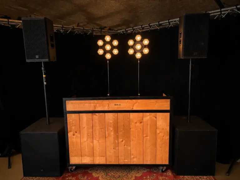 Houten DJ-booth met twee RCF KX-32A tops op subs en twee retrolampen, te huur bij dre-events